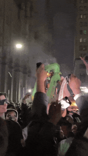 a crowd of people are gathered in a dark street with a man holding a green object
