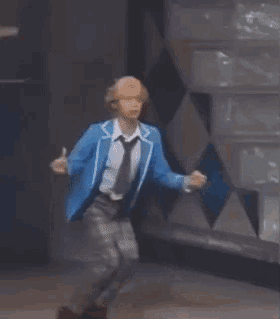 a man in a blue jacket and black pants is dancing on a stage .