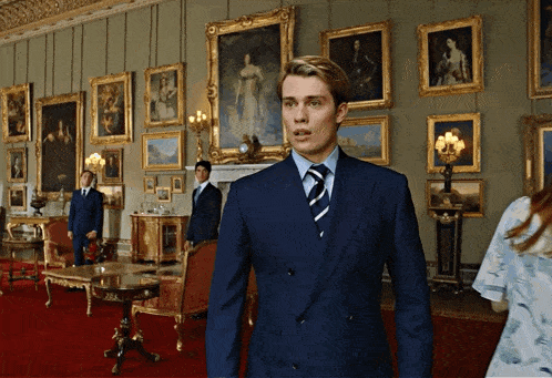 a man in a suit and tie stands in a room with paintings on the walls