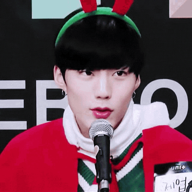 a young man wearing a headband and a red sweater is speaking into a microphone