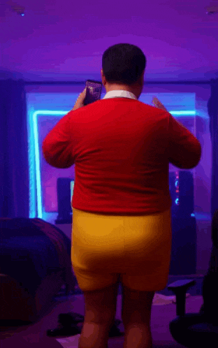 a man in a red sweater and yellow shorts is standing in a dark room