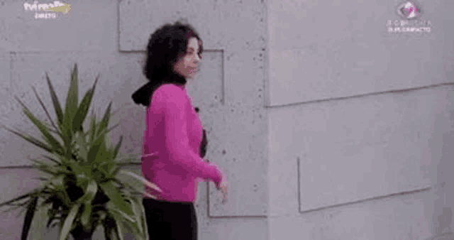 a woman in a pink sweater is standing in front of a concrete wall .