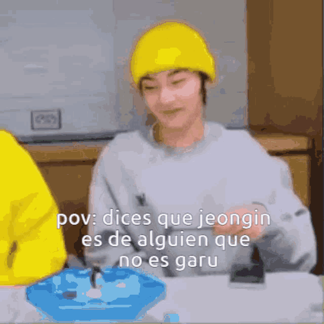 a man wearing a yellow hat is sitting at a table with a penguin toy .