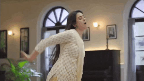 a woman in a white dress is dancing in a living room with her arms outstretched .