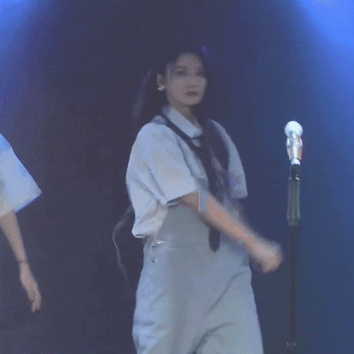 a woman wearing overalls and a tie is dancing in front of a microphone