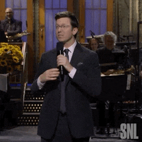 a man in a suit and tie is holding a microphone in front of a band .