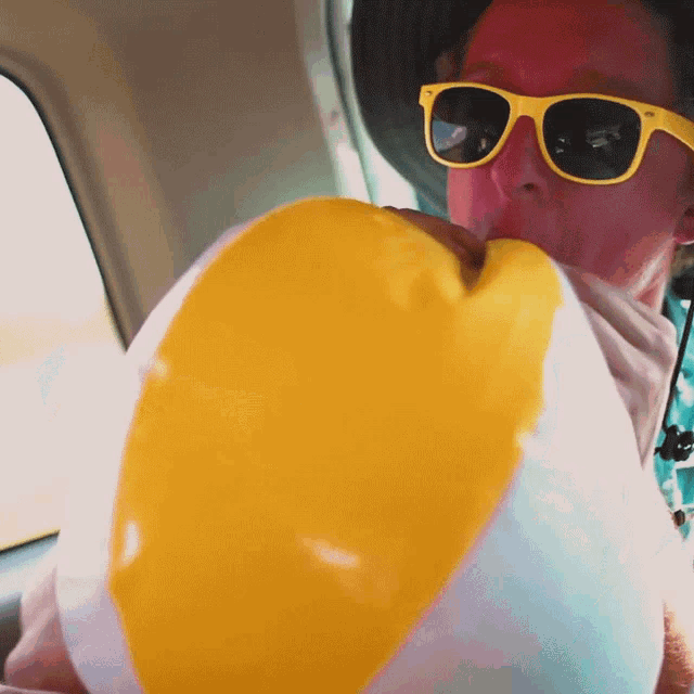 a person wearing sunglasses and a hat blows up a yellow beach ball