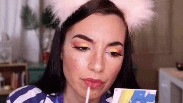 a woman wearing a cat ear headband is applying lip gloss with a straw .