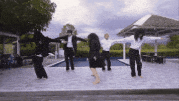 a group of people are dancing in front of a pool with their arms outstretched