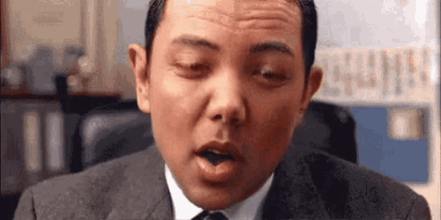 a man in a suit and tie is making a funny face while sitting in an office chair .