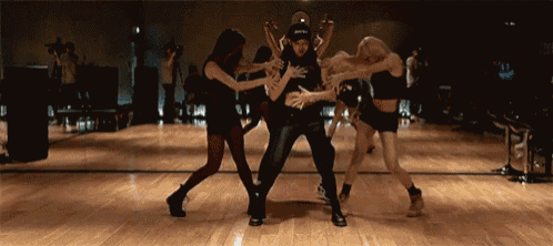 a group of women are dancing in front of a mirror and one of them is wearing a black hat that says sprite