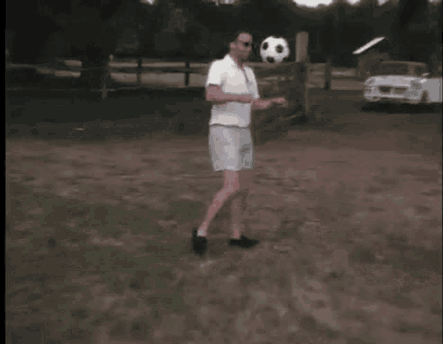 a man heads a soccer ball on his head in front of a white car