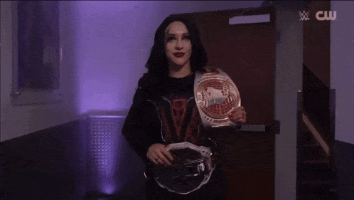a woman is holding a wrestling championship belt in a hallway with a cw logo in the background