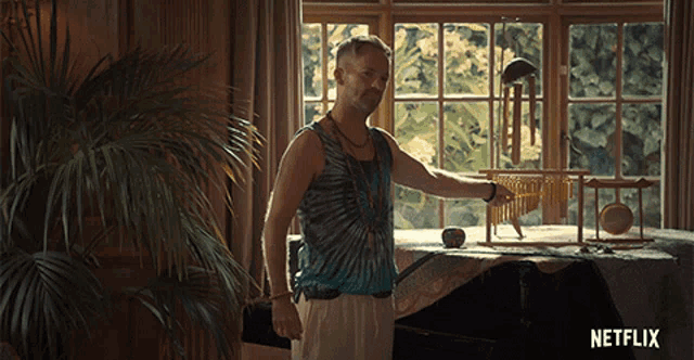 a man in a tie dye tank top stands in front of a window with a netflix logo on the bottom