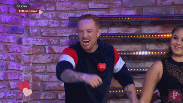 a man wearing a sweater that says " i love you " laughs in front of a brick wall