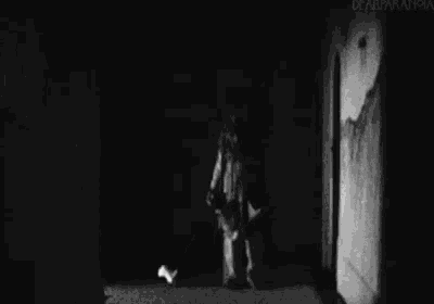 a black and white photo of a person standing in a hallway holding a vacuum cleaner .