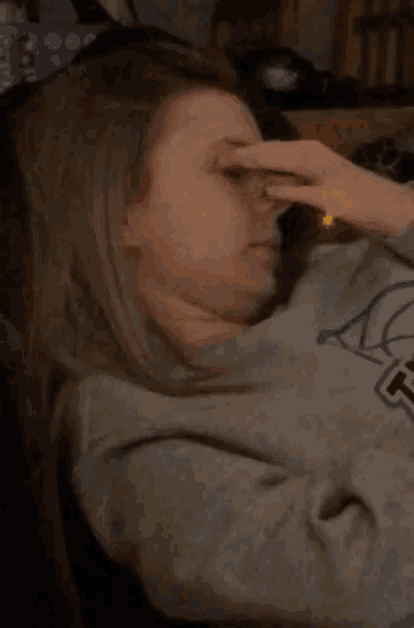 a woman wearing a sweatshirt with the letter t on it is rubbing her nose