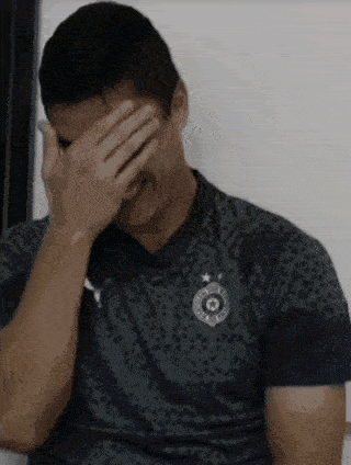 a man is covering his face with his hand while wearing a soccer jersey .