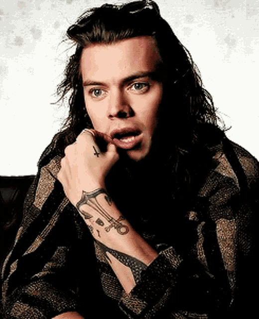 a young man with long hair has a tattoo on his wrist that says ' x '