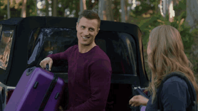 a man in a maroon sweater is carrying purple luggage