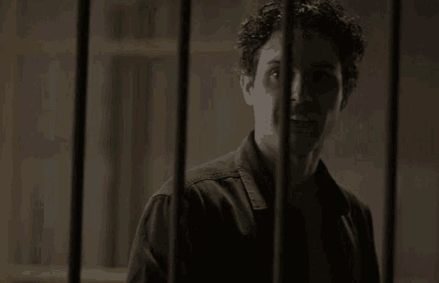 a man with curly hair is behind bars and looks at the camera