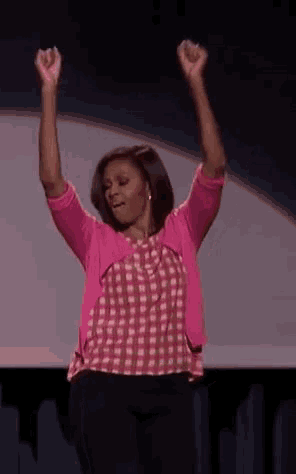 michelle obama is standing on a stage with her arms in the air and smiling .