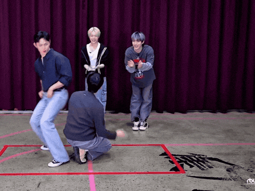 a group of young men are dancing in front of a red curtain