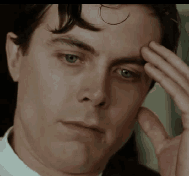 a close up of a man 's face with his hand to his forehead