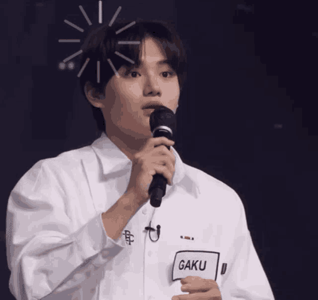a young man in a white shirt is holding a microphone and talking into it .