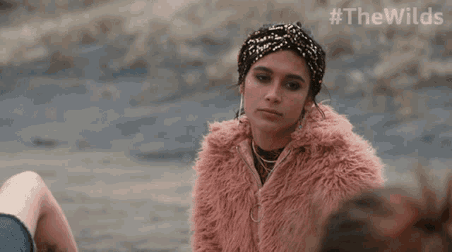 a woman wearing a headband and a pink fur coat is smiling with #thewilds written on the bottom