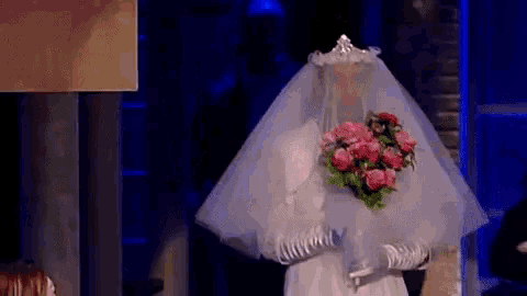 a man dressed as a bride is holding a bouquet of flowers .