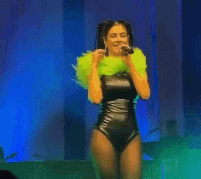 a woman is singing into a microphone while wearing a black bodysuit and a green feathered collar