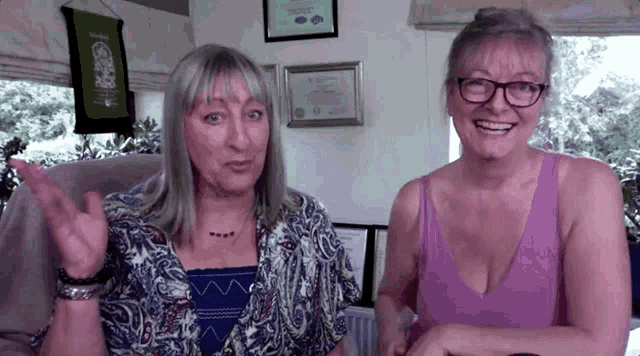 two women are sitting next to each other in a room and smiling .