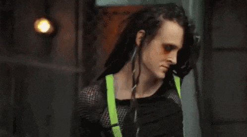 a woman with dreadlocks is standing in a dark room with her head down .