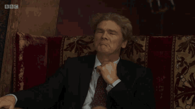 a man in a suit and tie sits on a couch with bbc written on the bottom right