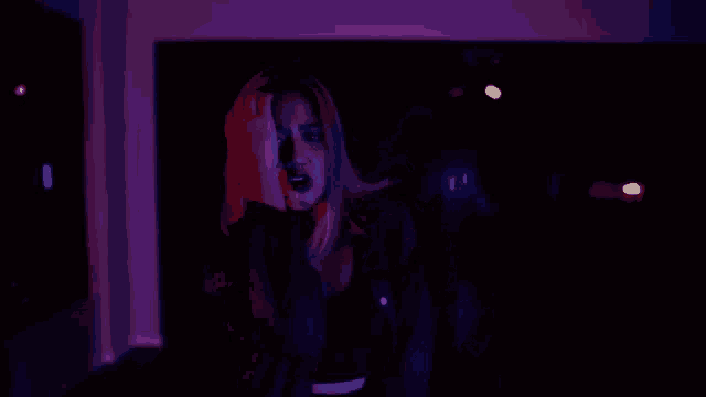 a woman is dancing in a dark room with purple lights behind her .