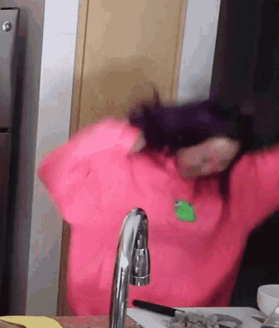 a woman in a pink sweater is standing in front of a sink .