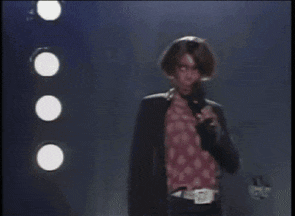 a woman singing into a microphone with a polka dot shirt on