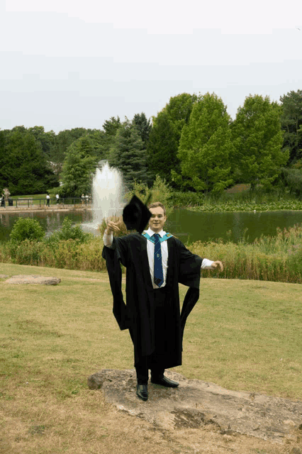 a man in a graduation cap and gown is standing in front of a lake