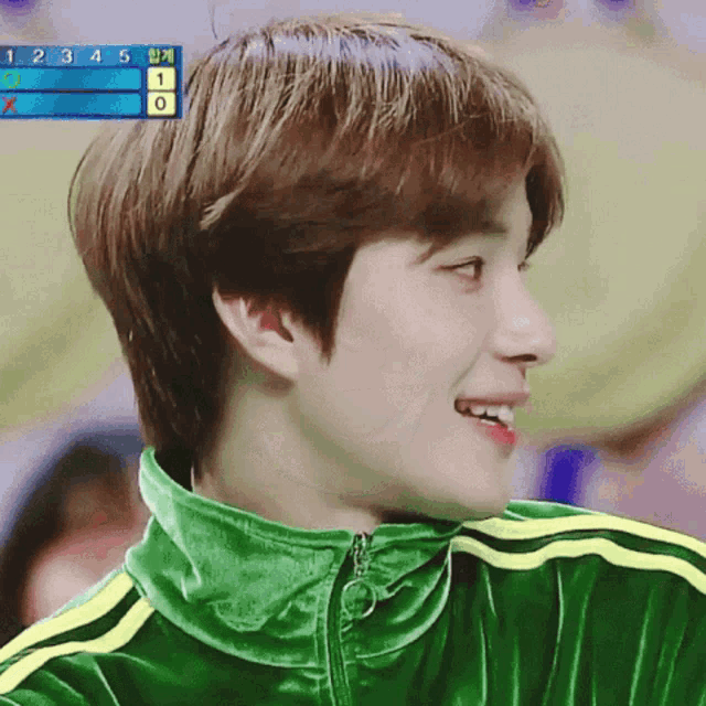 a young man wearing a green jacket with yellow stripes is smiling in front of a scoreboard that says 1 2 3 4 5