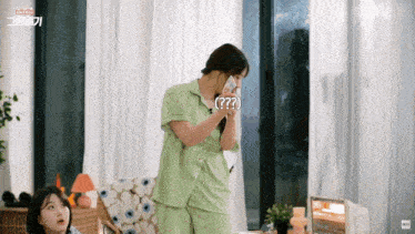 a woman in a green pajama set is talking on a cell phone while another woman looks on .