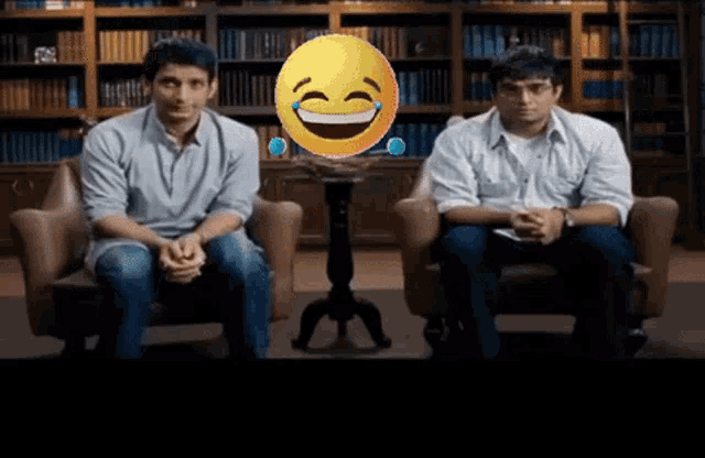 two men are sitting in chairs in front of a laughing smiley face