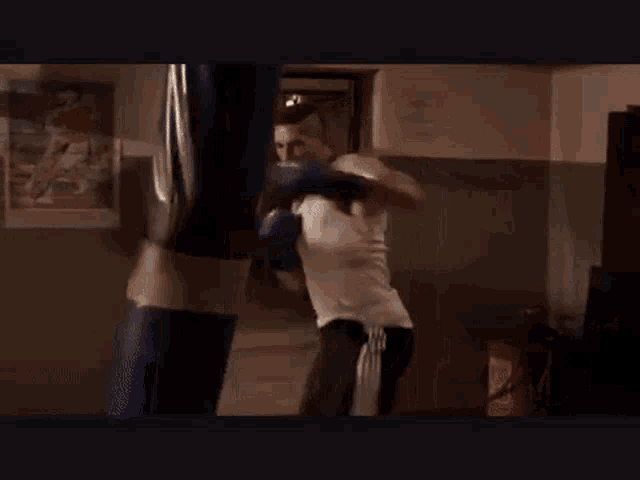 a man in a white tank top is boxing with a blue punching bag in a gym .