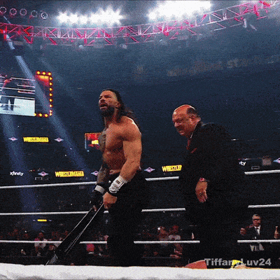 a man in a suit stands next to a wrestler in a ring with xfinity written on the wall behind him