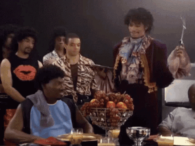 a group of people sitting around a table with a bowl of fruit on it