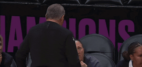 a man talks to a woman in front of a purple banner that says champions