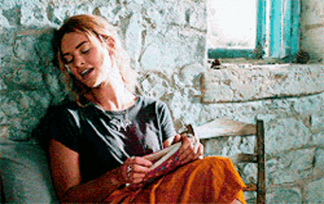 a woman is sitting on a couch reading a book .