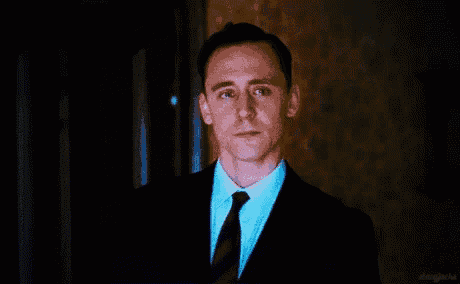 a man in a suit and tie is looking at the camera in a dark room .