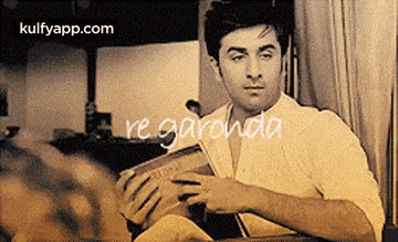 a man is sitting at a table reading a book with the words regardda written on the bottom .