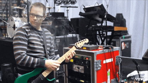 a man playing a green guitar in front of a red box that says vevo on it